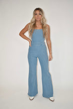 Load image into Gallery viewer, women&#39;s clothing boutique, model is modeling a light wash denim jumpsuit that has flare legs and an open back
